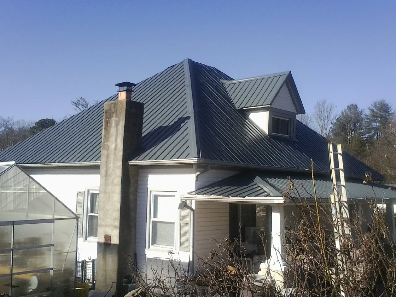 Dark blue standing seam metal roof on a white farmhouse with dormer — Slate & Tile Roof Repair by Roofing Brothers in Center Barnstead