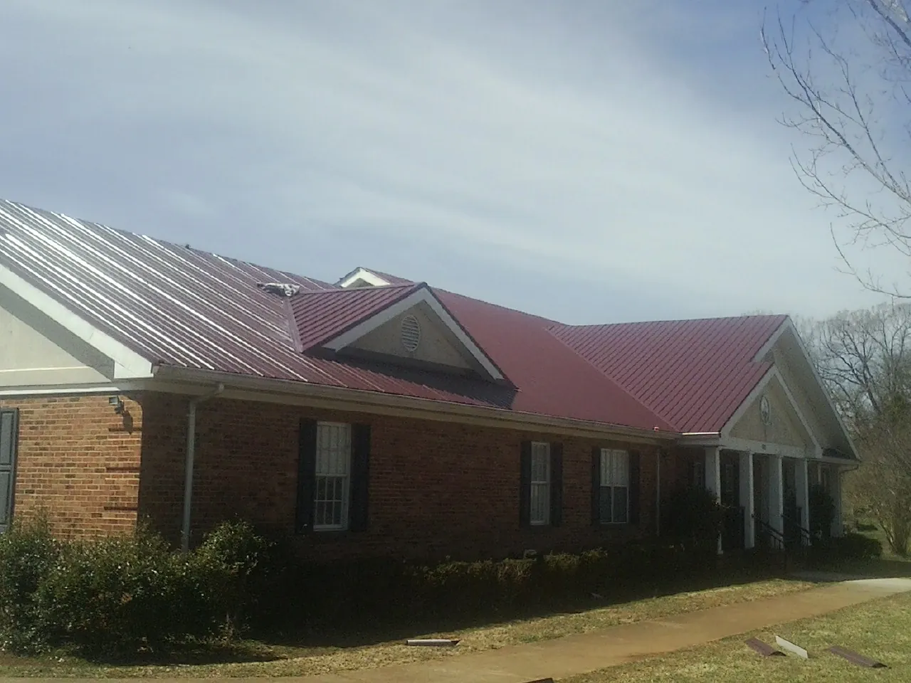 Red metal roof with gabled entries on a long brick building, from a Hail Damage Roof Repair job in Center Barnstead