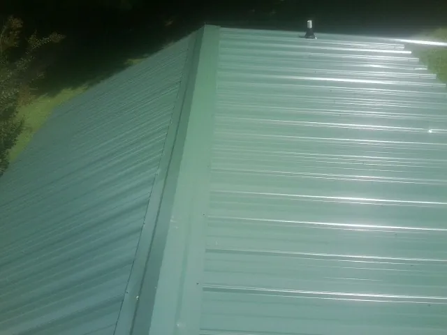 New green metal panels meeting at the ridge of a roof — Flat Roof Repair work by our crew in Center Barnstead