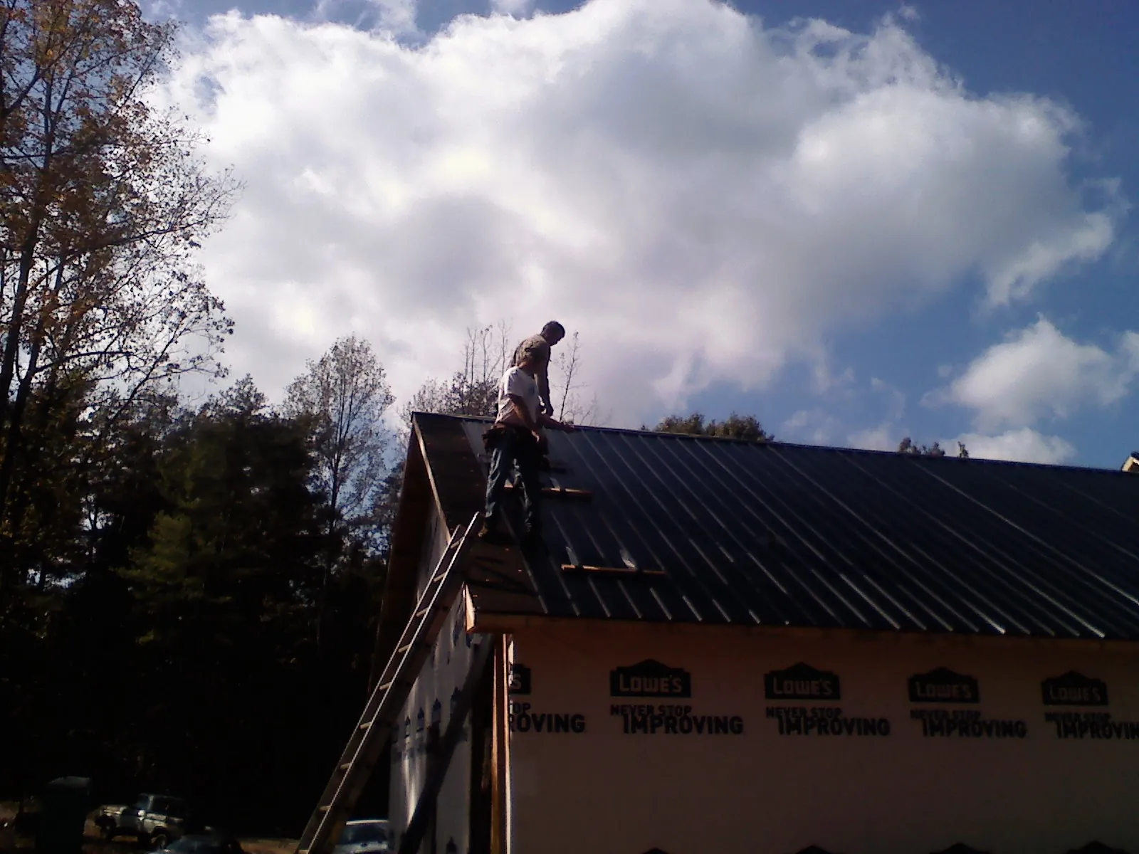 Roofer fastening dark metal panels high against a cloudy sky, from a Roof Inspection job in Center Barnstead