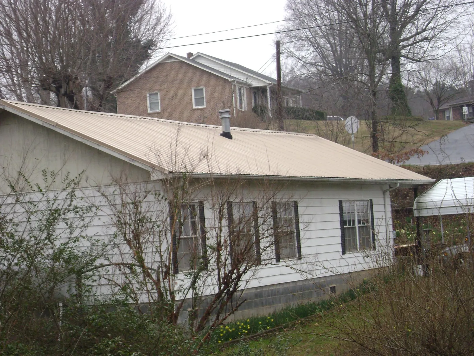 Tan metal roof on a white sided house set into a hillside — Commercial Roofing by Roofing Brothers in Center Barnstead