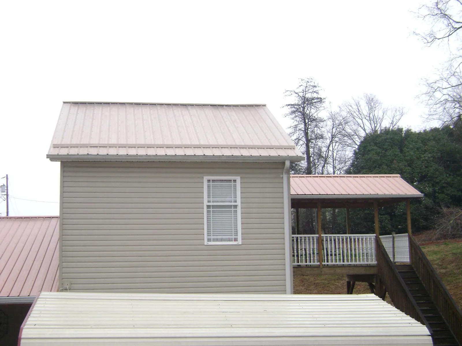 Tan metal roofs on a two story addition and attached porch, from a Roof Replacement job in Center Barnstead